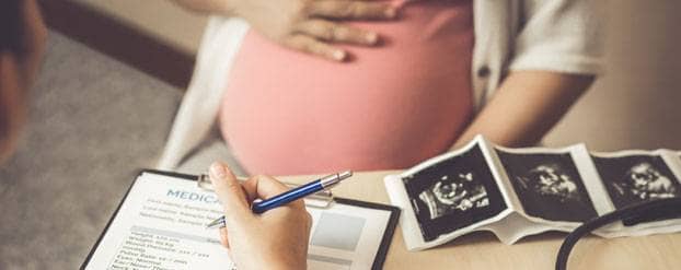 Foto Zwangere vrouw bij dokter met vragenlijst en echo op bureau
