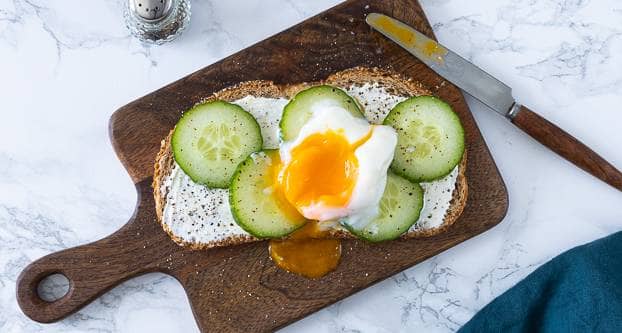 Foto boterham met gepocheerd ei op houten plank met komkommerschijfjes