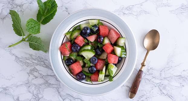 Schaal met fruitsalade van watermeloen, komkommer, blauwe bessen en munt.