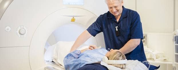 Een vrouw gaat met een koptelefoon op een MRI-scan in, terwijl de arts haar in het apparaat schuift.