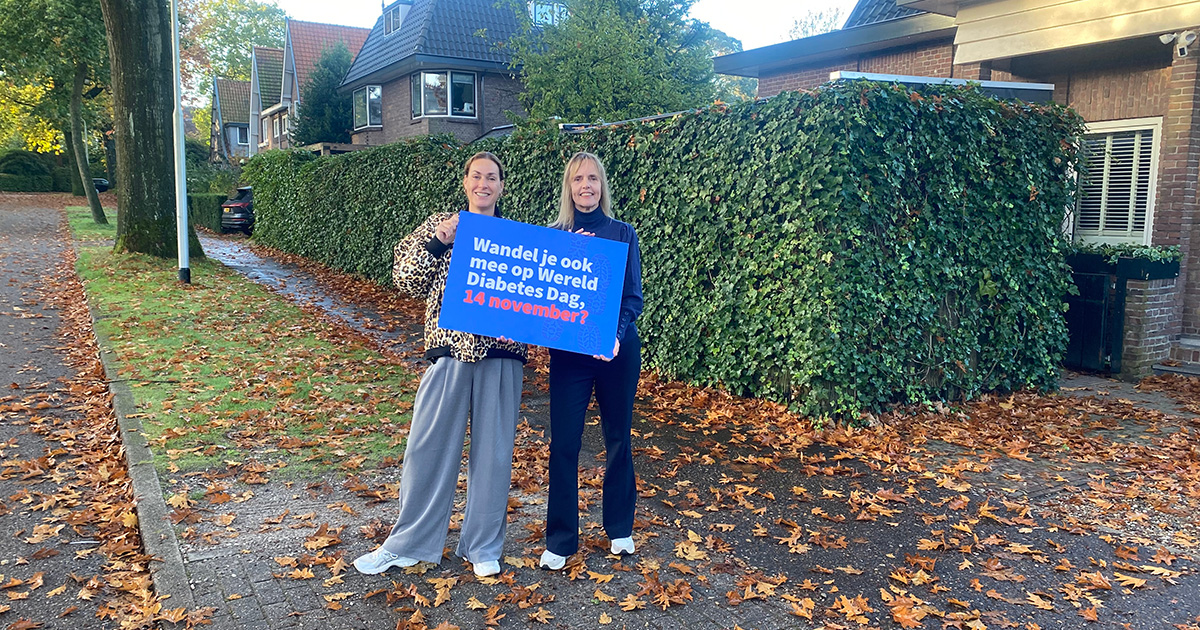 Twee mensen op straat met bord om promotie te maken voor Half uurtje door het buurtje