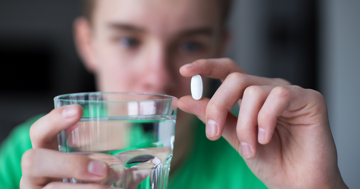 Jongen houdt witte pil in zijn ene hand en glas water in zijn andere hand