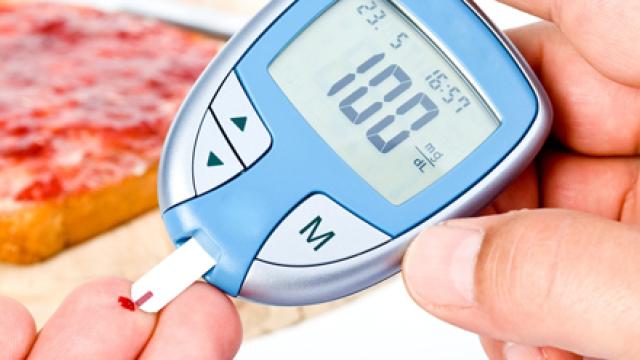 Een hand waarbij één van de vingers een druppel bloed heeft, terwijl de andere hand een glucosemeter vasthoudt die de bloedsuikerwaarde meet.