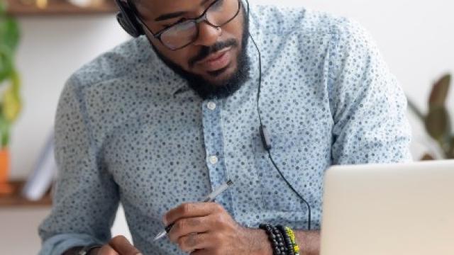 Man volgt webinar op zijn laptop en maakt aantekeningen