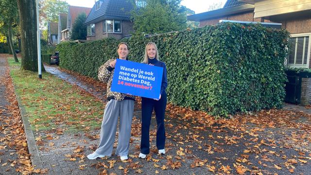 Twee mensen op straat met bord om promotie te maken voor Half uurtje door het buurtje 