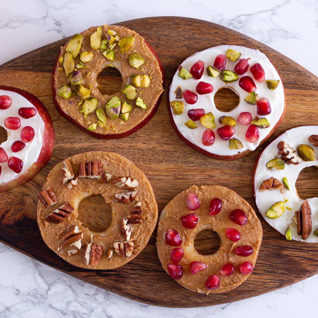 Met  pindakaas, noten en granaatappelpitten versierde appelplakjes