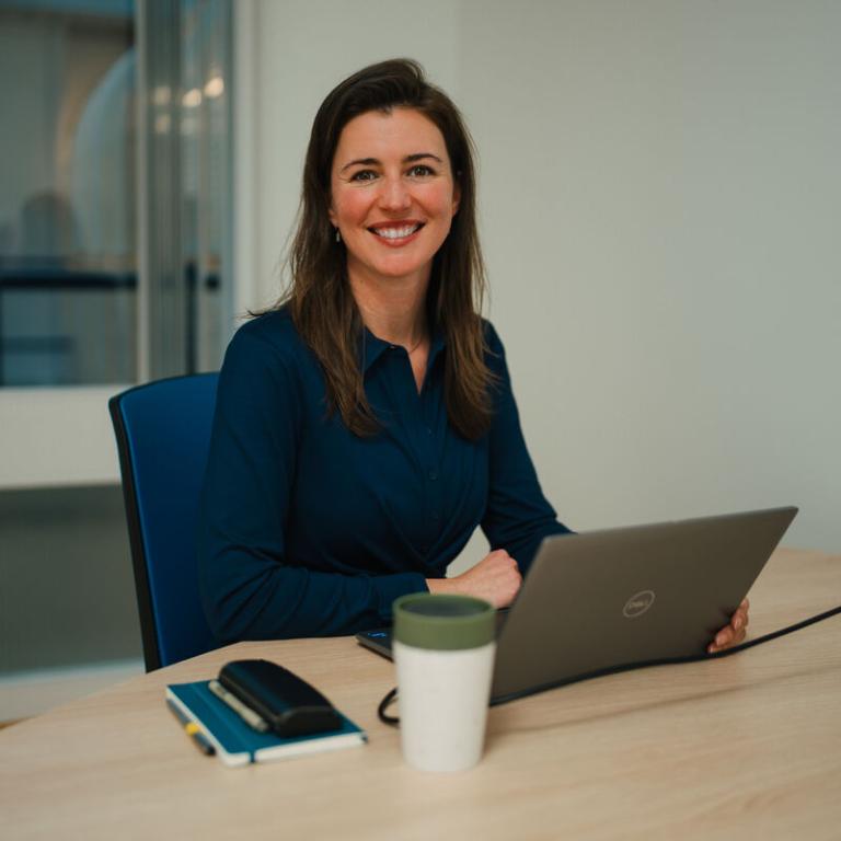 Onderzoeker Marleen Kunneman zit achter haar laptop en lacht naar de camera