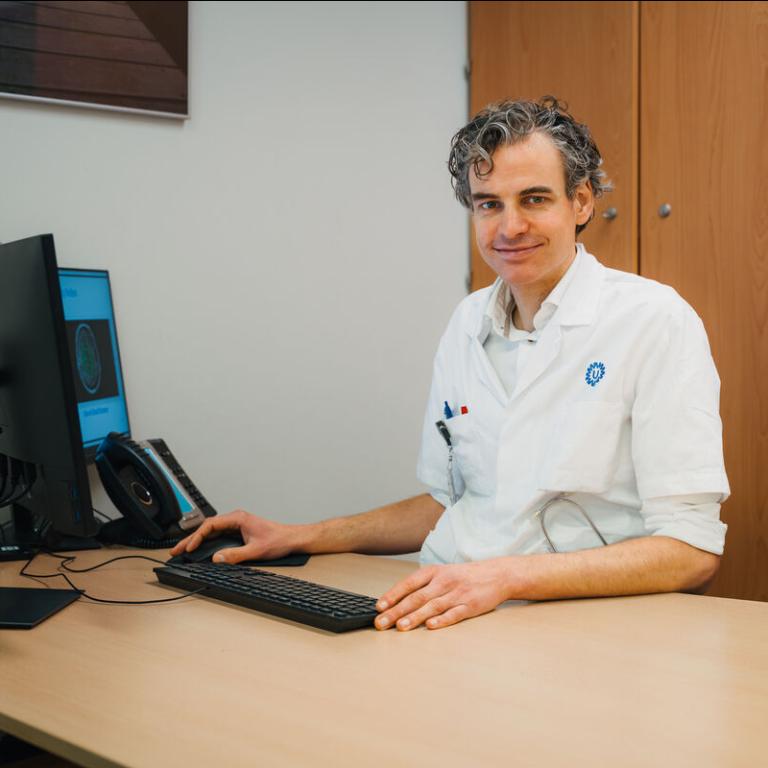 Onderzoeker Thomas van Sloten zit aan zijn bureau en glimlacht naar de camera