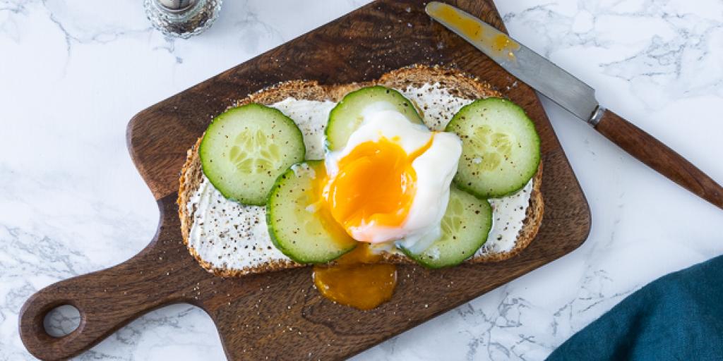 Foto boterham met gepocheerd ei op houten plank met komkommerschijfjes