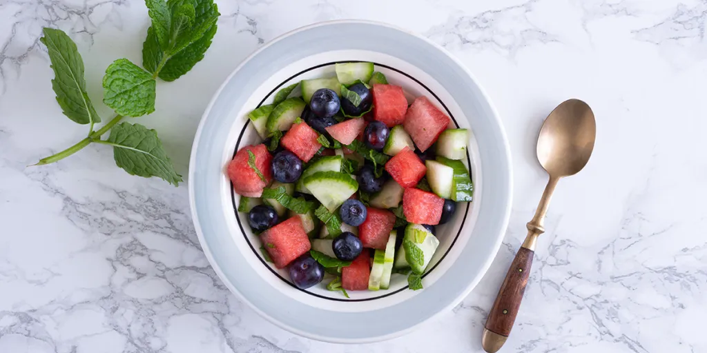 Schaal met fruitsalade van watermeloen, komkommer, blauwe bessen en munt.