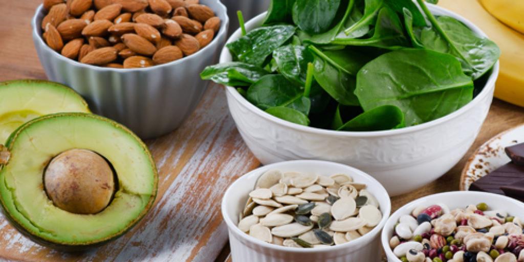 Een compositiefoto van bananen, pure chocolade, avocado, opgesteld met schaaltjes vol gezonde voeding: spinazie, amandelen, pitten, zaden en yoghurt