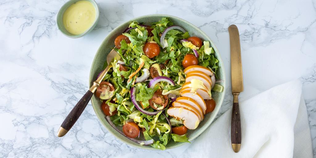 Salade tomaatjes, rode ui en reepjes gerookte kip en bakje met mosterddressing ernaast