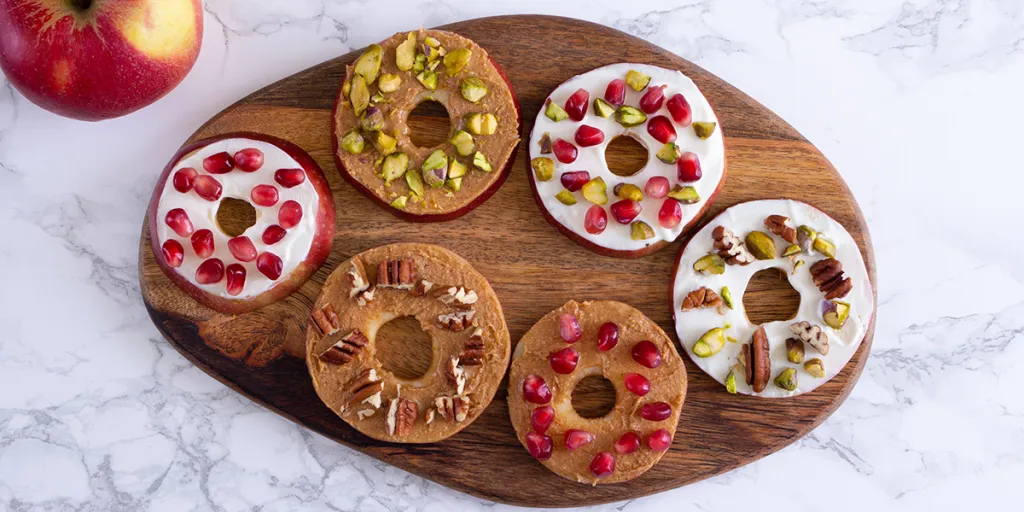 Met  pindakaas, noten en granaatappelpitten versierde appelplakjes