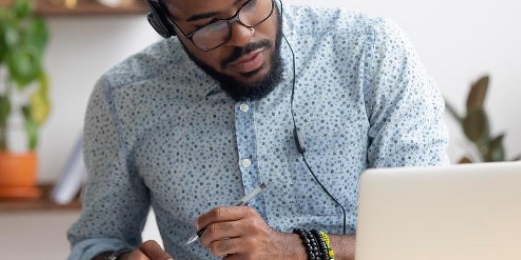 Man volgt webinar op zijn laptop en maakt aantekeningen