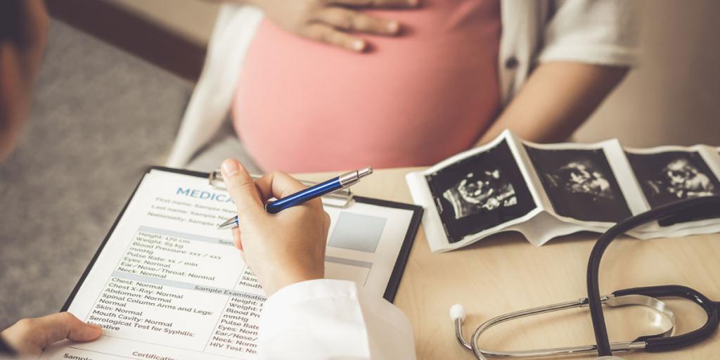 Foto Zwangere vrouw bij dokter met vragenlijst en echo op bureau