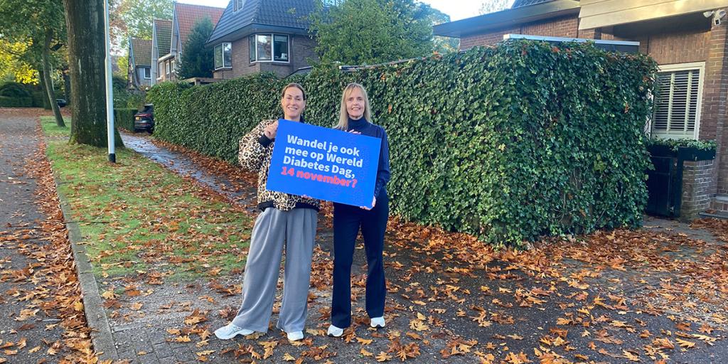 Twee mensen op straat met bord om promotie te maken voor Half uurtje door het buurtje 