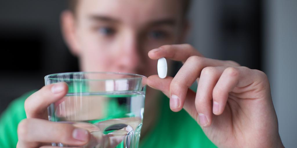 Jongen houdt witte pil in zijn ene hand en glas water in zijn andere hand