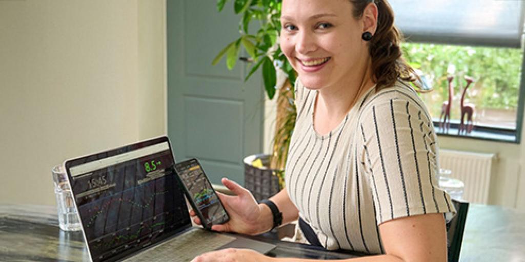 Jonge vrouw zit achter laptop met mobiel en bekijkt haar bloedsuikerwaarden