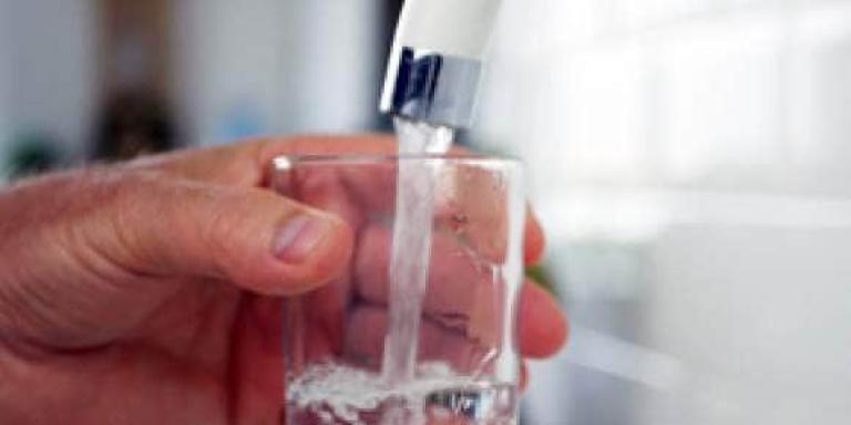 Hand houdt glas water vast onder een lopende kraan