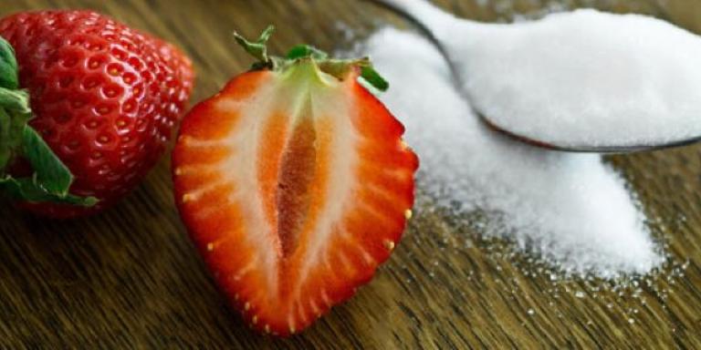 Lepel met witte suiker naast een aardbei