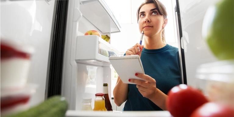 Foto van vrouw die aantekeningen maakt in de keuken achter haar laptop