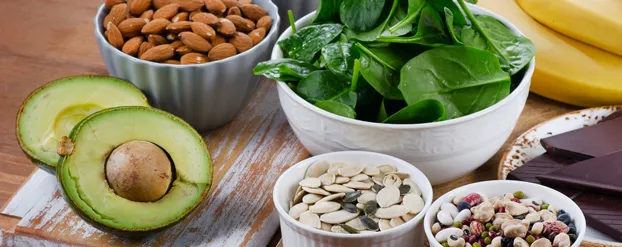 Een compositiefoto van bananen, pure chocolade, avocado, opgesteld met schaaltjes vol gezonde voeding: spinazie, amandelen, pitten, zaden en yoghurt