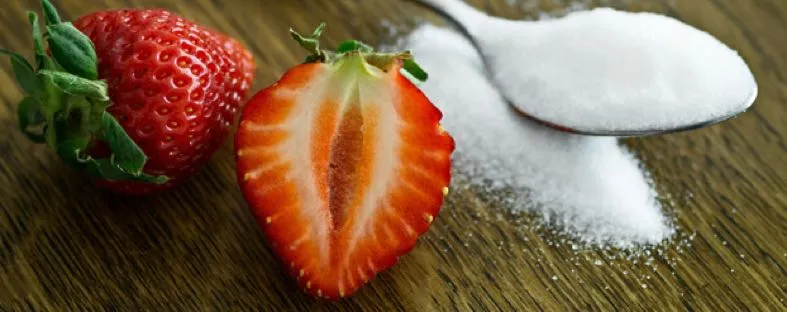 Lepel met witte suiker naast een aardbei