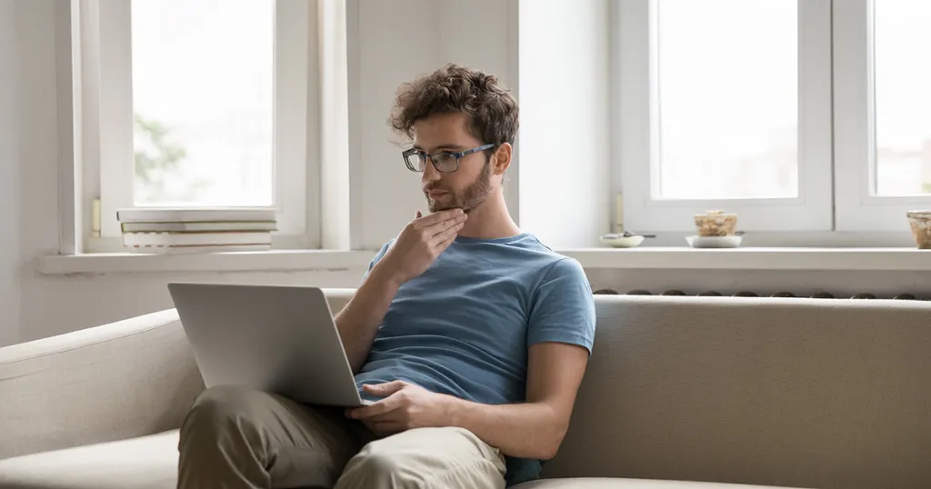Vragend kijkende man achter laptop op de bank