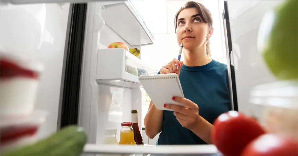 Foto van vrouw die aantekeningen maakt in de keuken achter haar laptop